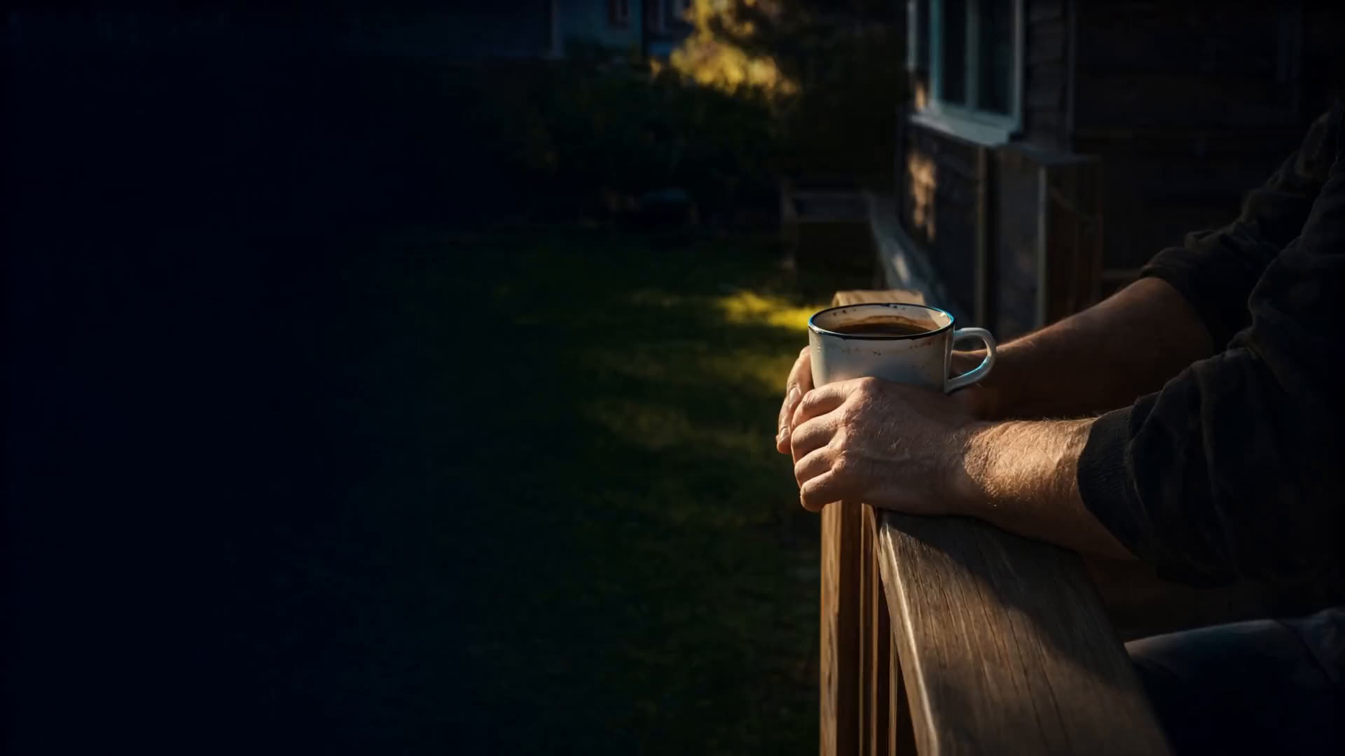 Hands resting on a deck railing with coffee at sunset